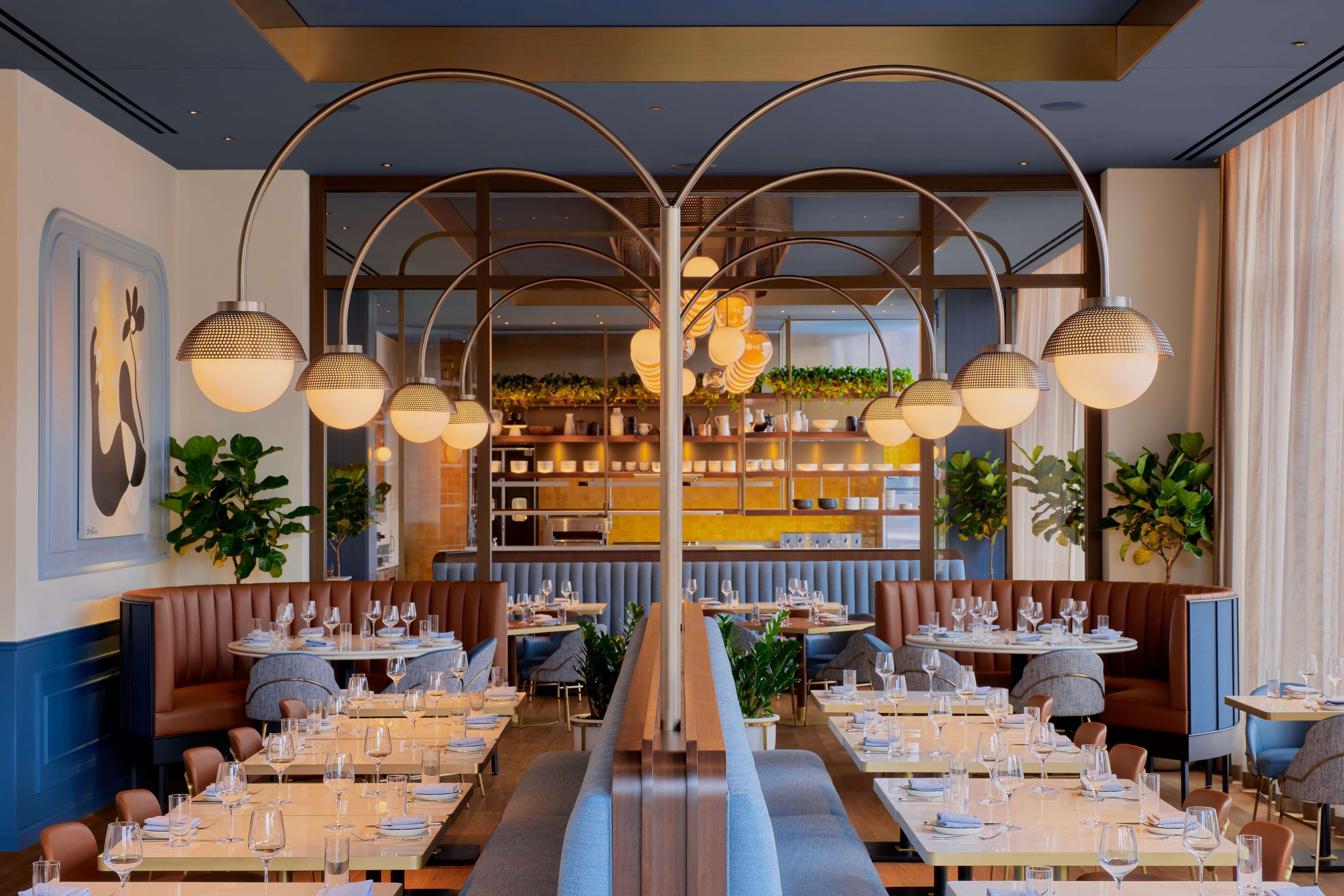 Um restaurante com uma mesa central comprida, cabines de cada lado e luminárias pendentes.