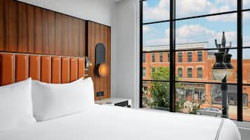 Habitación de hotel con un ventanal grande, cabecera de madera y vistas a una calle de la ciudad.