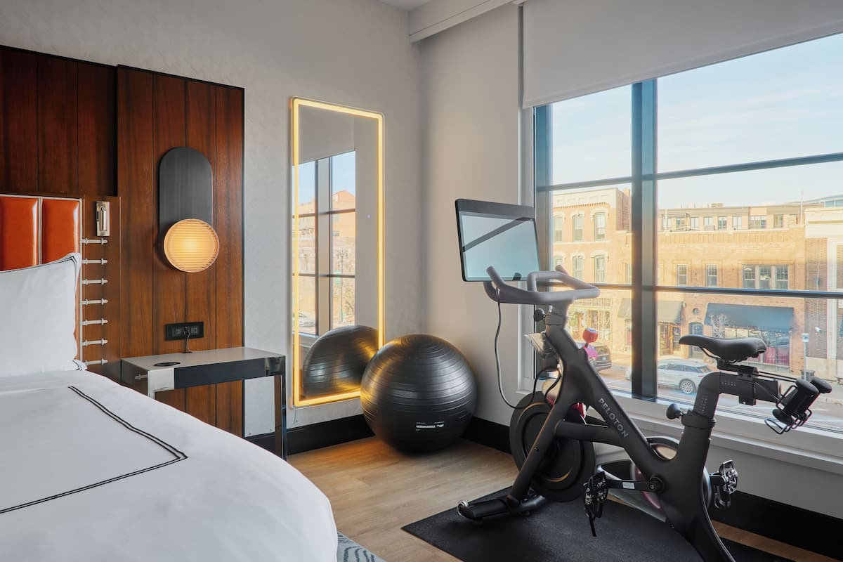 A hotel room with a bed, exercise equipment, a large mirror, and a view of the city through the window.