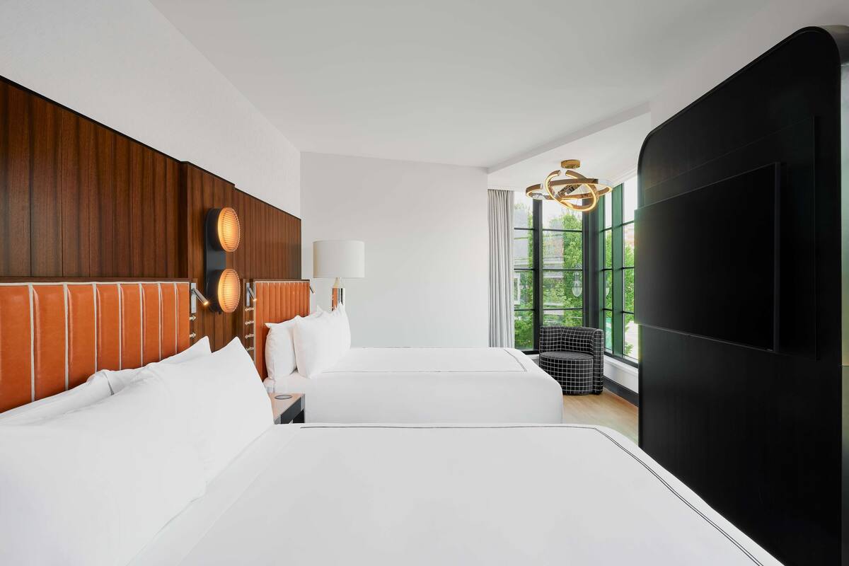 A hotel room with two beds, a large window, a TV, and a chandelier.