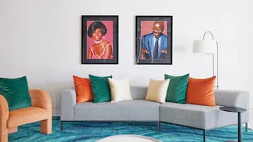 A modern living room with a grey sofa, colorful cushions, a round coffee table, and two framed artworks on the wall.