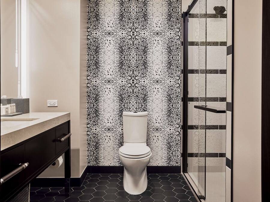 A modern bathroom with a white toilet, a black and white speckled wall, a glass shower enclosure, and a dark tiled floor.