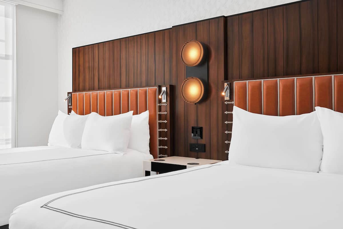A hotel room with two beds, wooden headboards, and wall-mounted lighting.