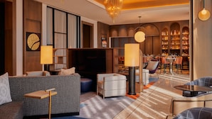 Un hall d’hôtel moderne avec un canapé, des fauteuils, un téléviseur et un coin bar.