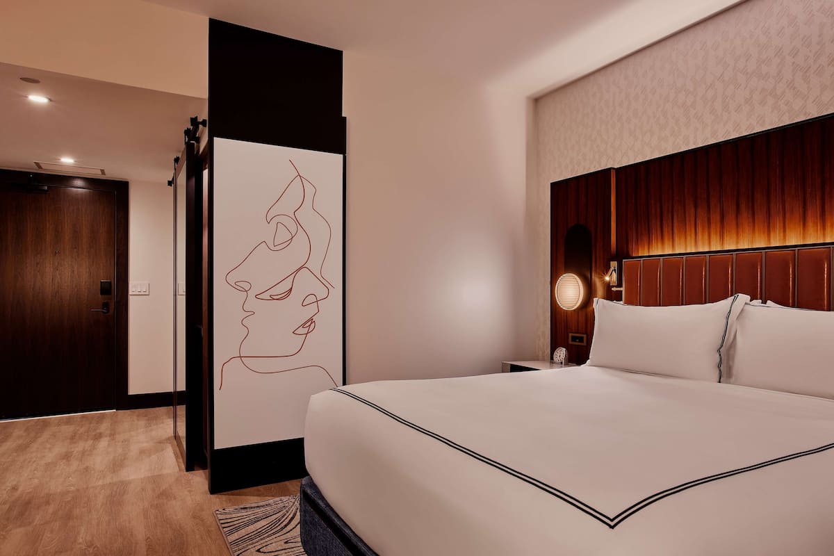 A hotel room with a large bed, a wooden headboard, a wall art piece, and a door.