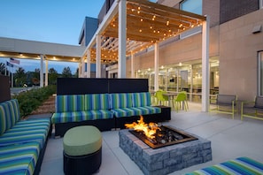 An outdoor seating area with a fire pit, cushioned seating, and a covered patio with string lights. - Home2 Suites By Hilton Grand Rapids Airport (Grand Rapids)