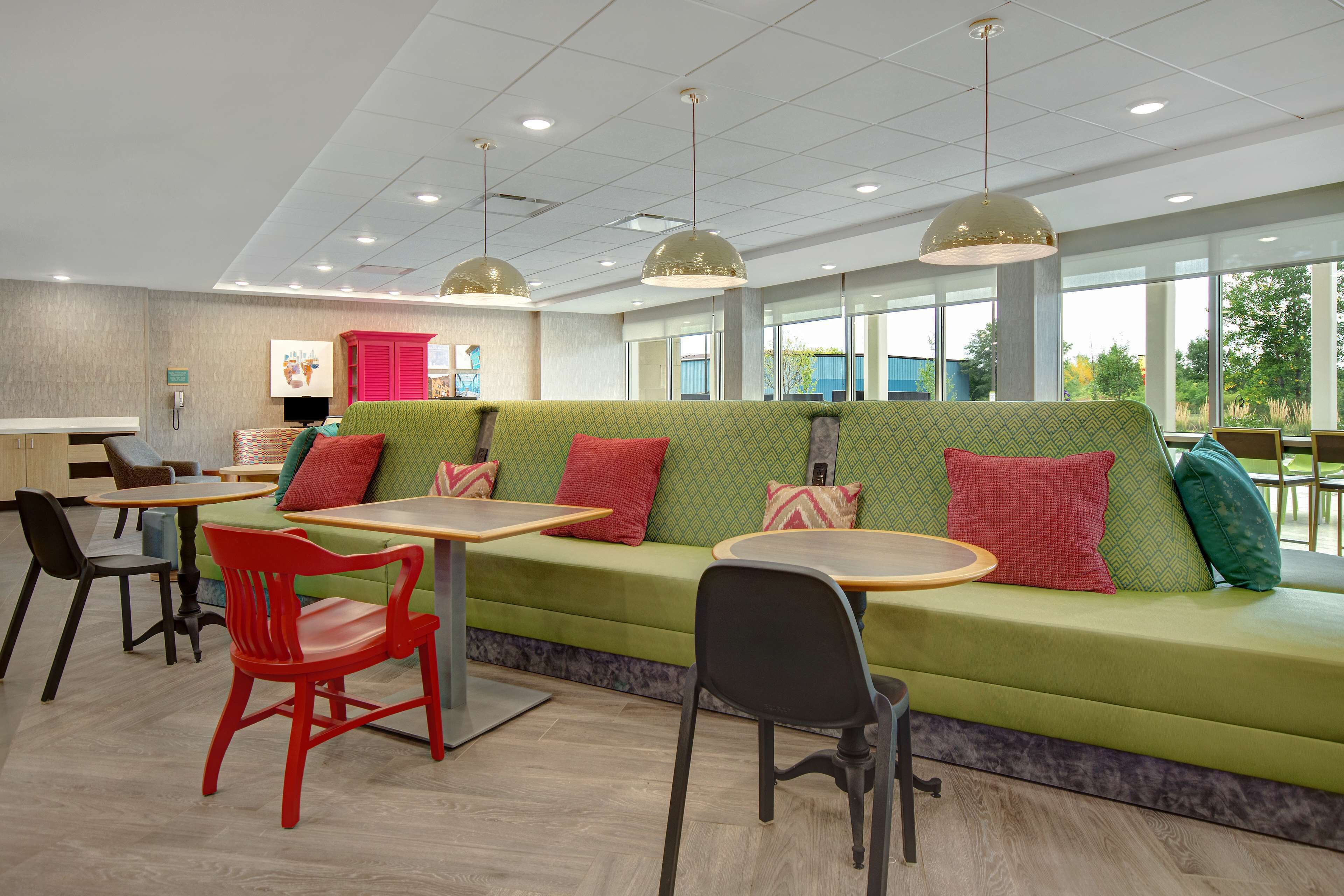 Un espace de détente intérieur moderne, avec des canapés verts, des chaises rouges et des tables rondes.