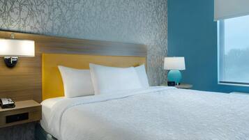 Una cama bien hecha con sábanas blancas, cabecera de madera y mesita de noche con lámpara y teléfono.