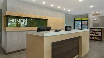 A hotel reception desk with a digital screen, a refrigerator with beverages, and a snack bar.