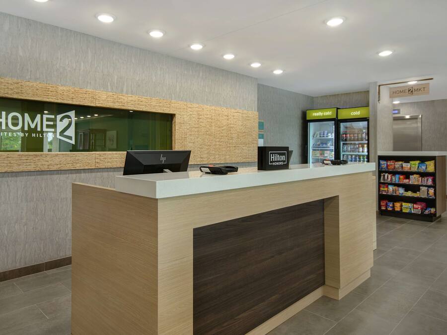 A hotel reception desk with a digital screen, a refrigerator with beverages, and a snack bar.