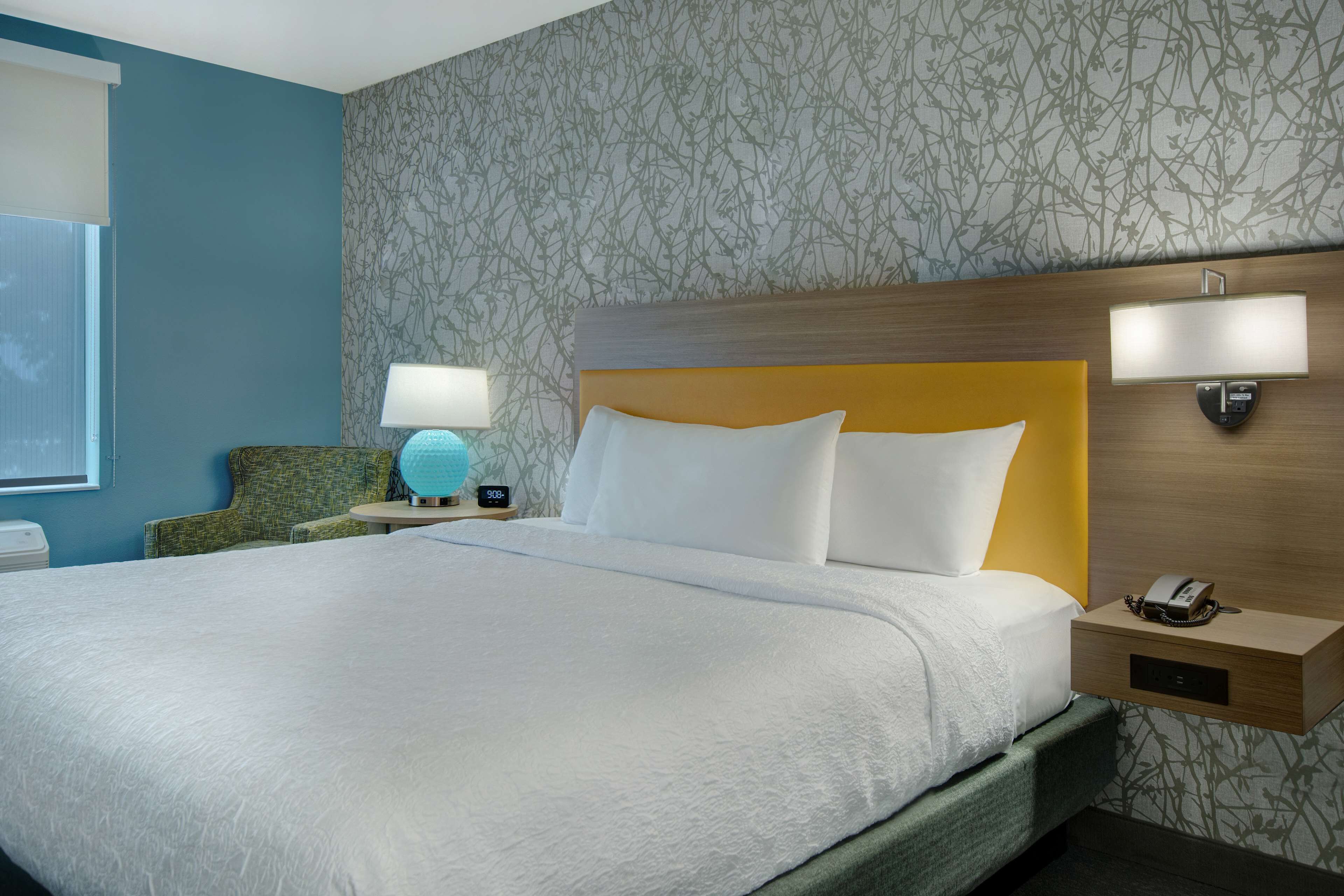 Een hotelkamer met een groot bed, een nachtkastje met een lamp, een telefoon en een wandlamp.
