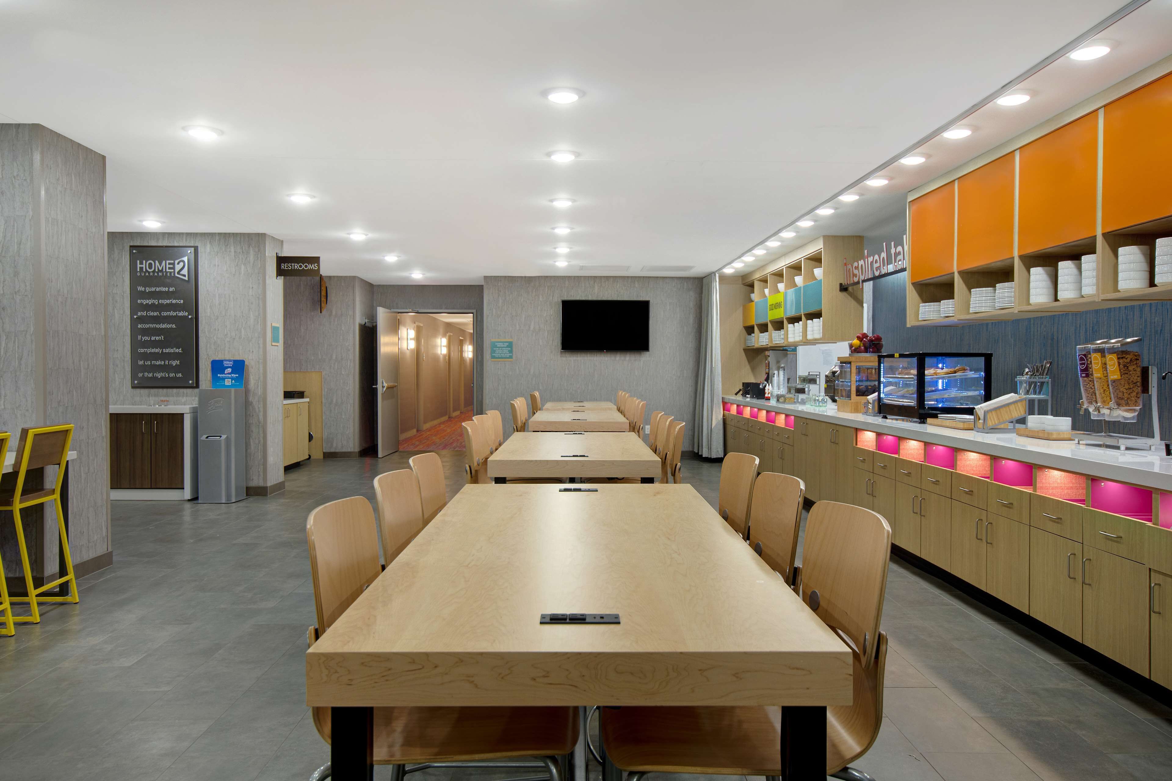 Un hall d’hôtel moderne avec un long comptoir d’accueil, un téléviseur fixé au mur et un présentoir proposant divers produits et services.