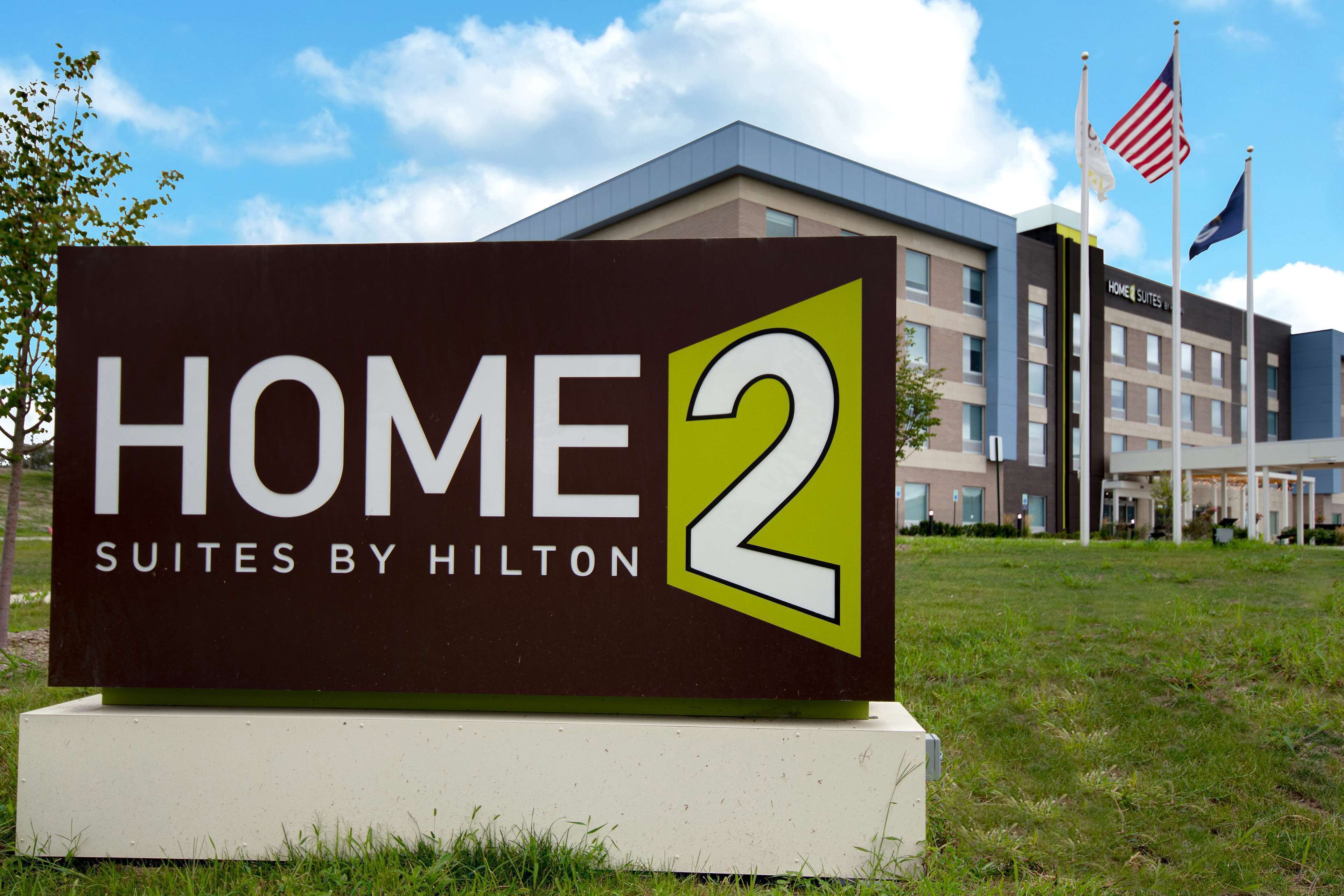 A sign for 'HOME 2 Suites by Hilton' with a modern building in the background.