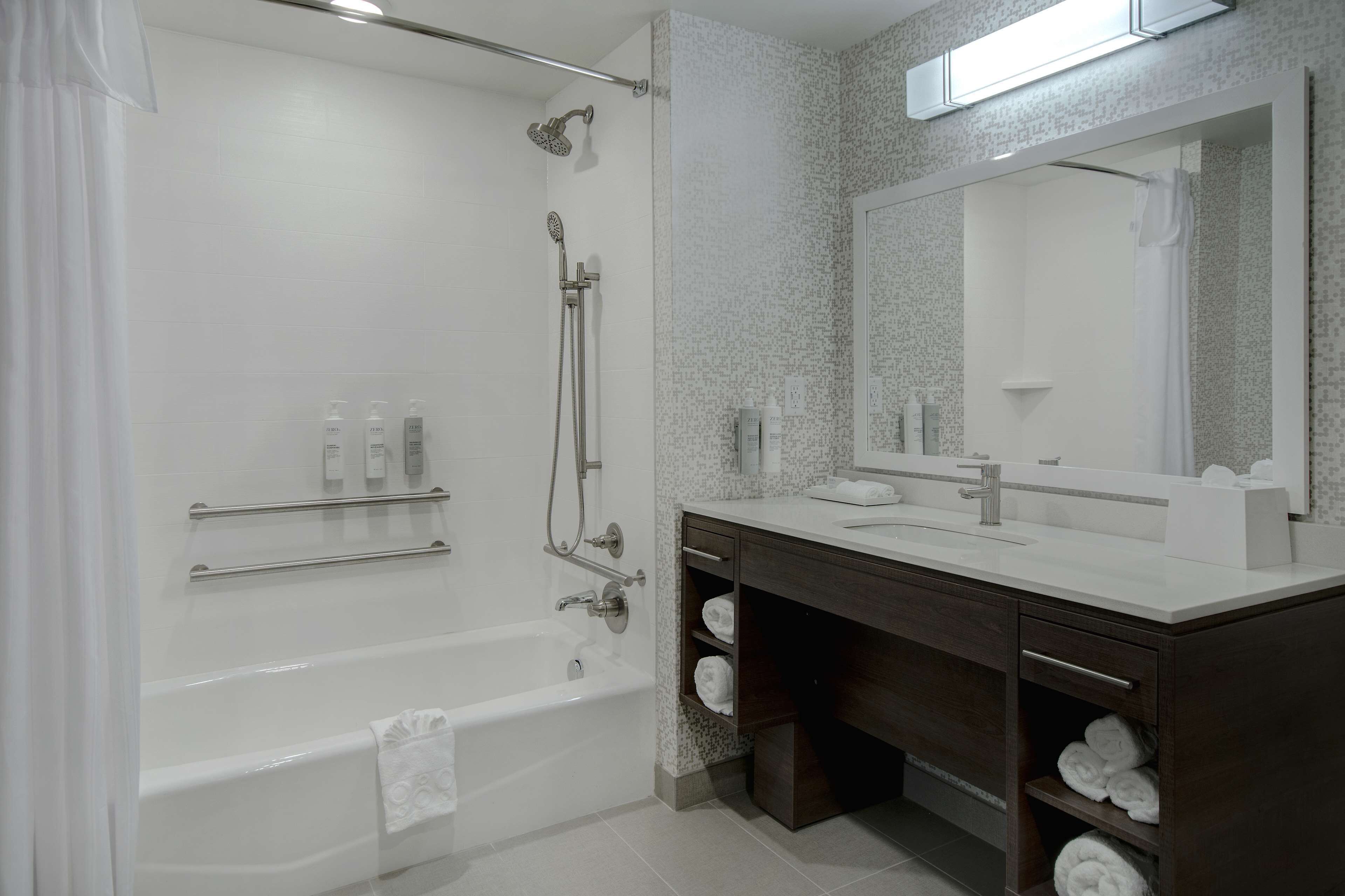 Ein modernes Badezimmer mit einer Badewanne, einer Dusche, einem Waschtisch mit Spiegel und Regalen mit Handtüchern.