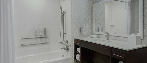 Ein modernes Badezimmer mit einer Badewanne, einer Dusche, einem Waschtisch mit Spiegel und Regalen mit Handtüchern.