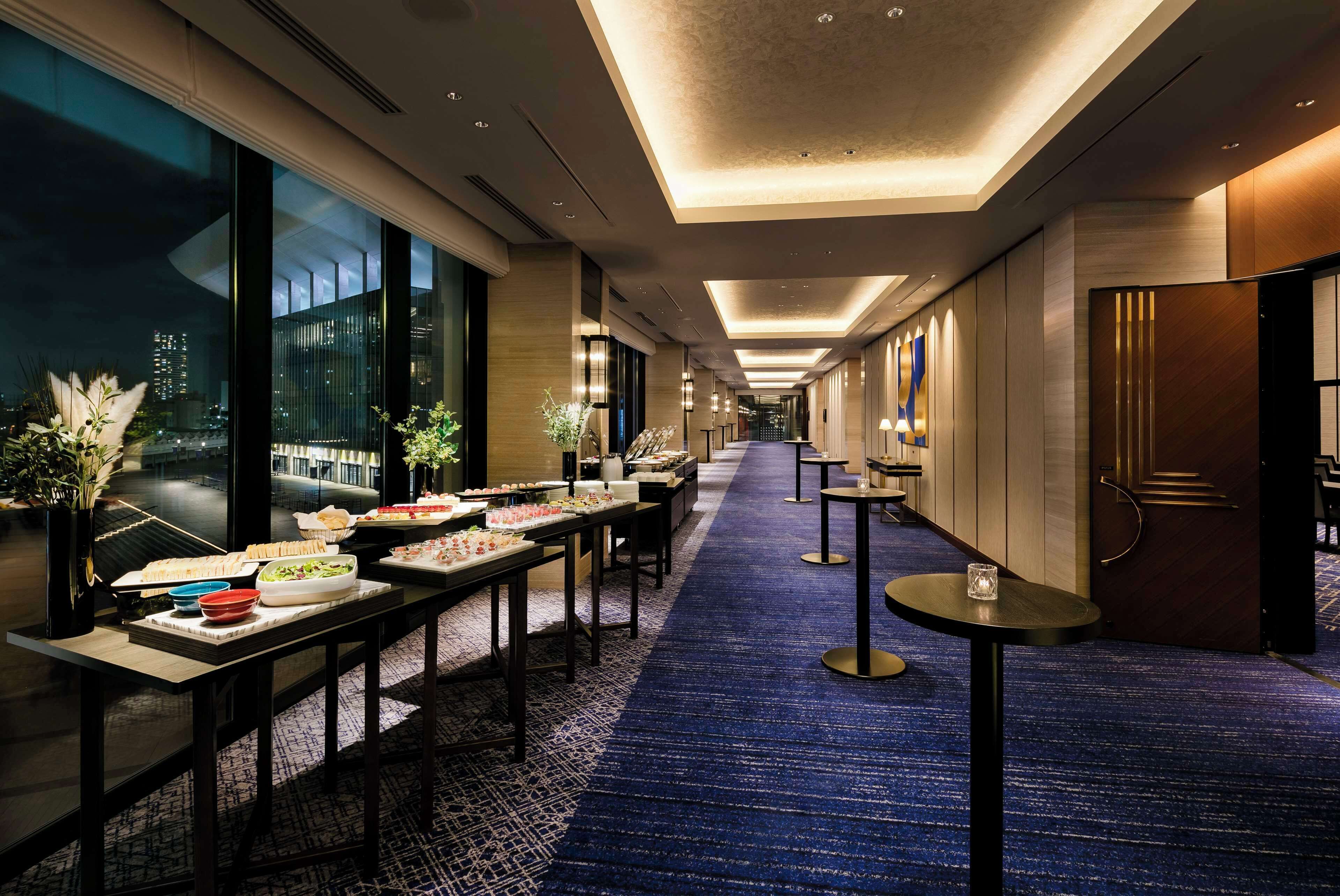 A hotel corridor with tables set up for a buffet, featuring various food items and a blue carpet.