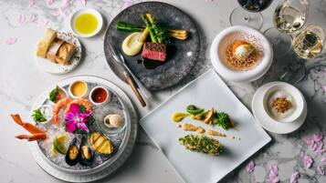 A variety of dishes on plates, including seafood, vegetables, and a steak, with wine glasses and a dessert on the side.