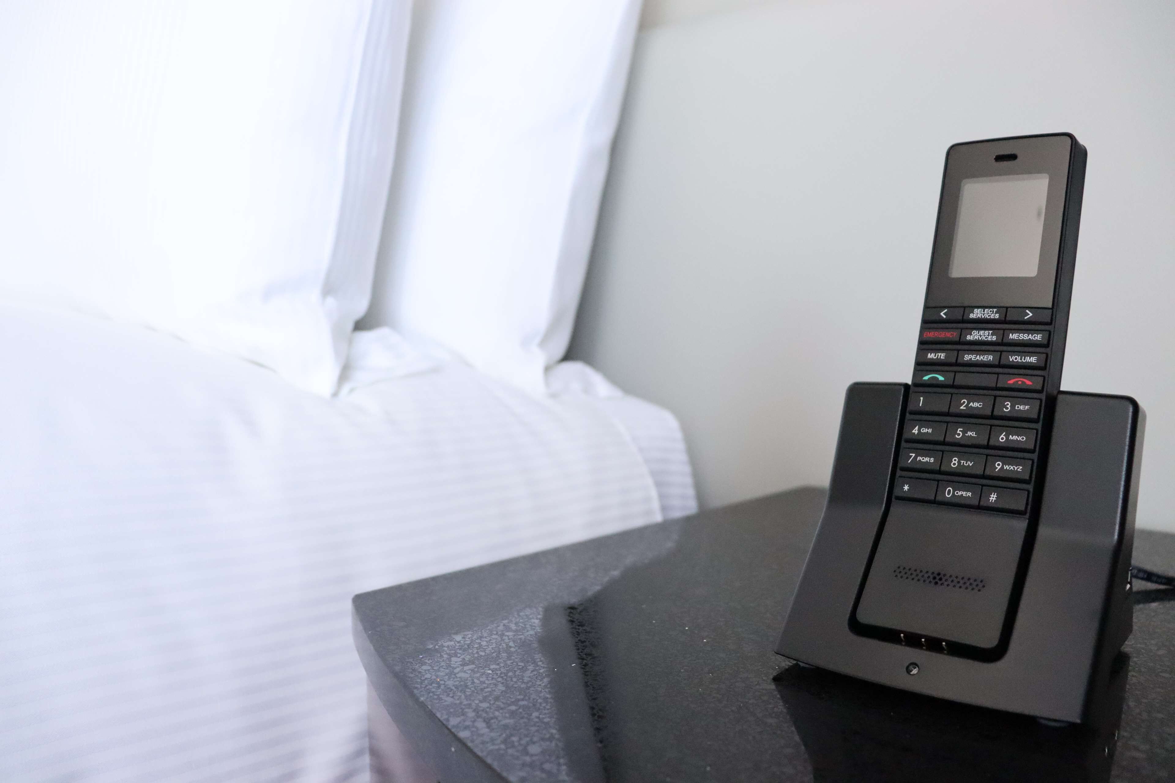 A hotel room with a bedside telephone and a bed with white bedding.