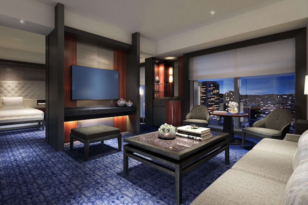 Quarto de hotel moderno com cama, área de estar e vista para a cidade.