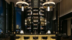 A modern bar area with a central liquor display, seating arrangements, and a city view.
