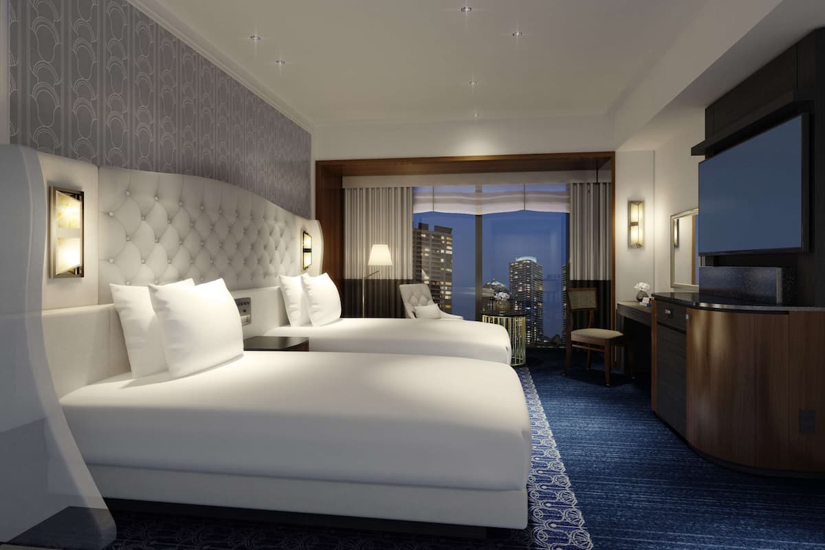 Quarto de hotel com duas camas, uma escrivaninha, televisão e vista para a cidade.