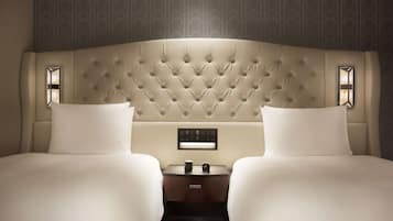 A hotel room with a tufted headboard, two beds, a nightstand with a clock, and a control panel.