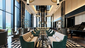 A spacious lobby with a grand piano, plush seating, and a central bar area.