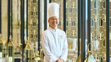 A person in a chef's uniform standing in front of a decorative interior with patterned metalwork.