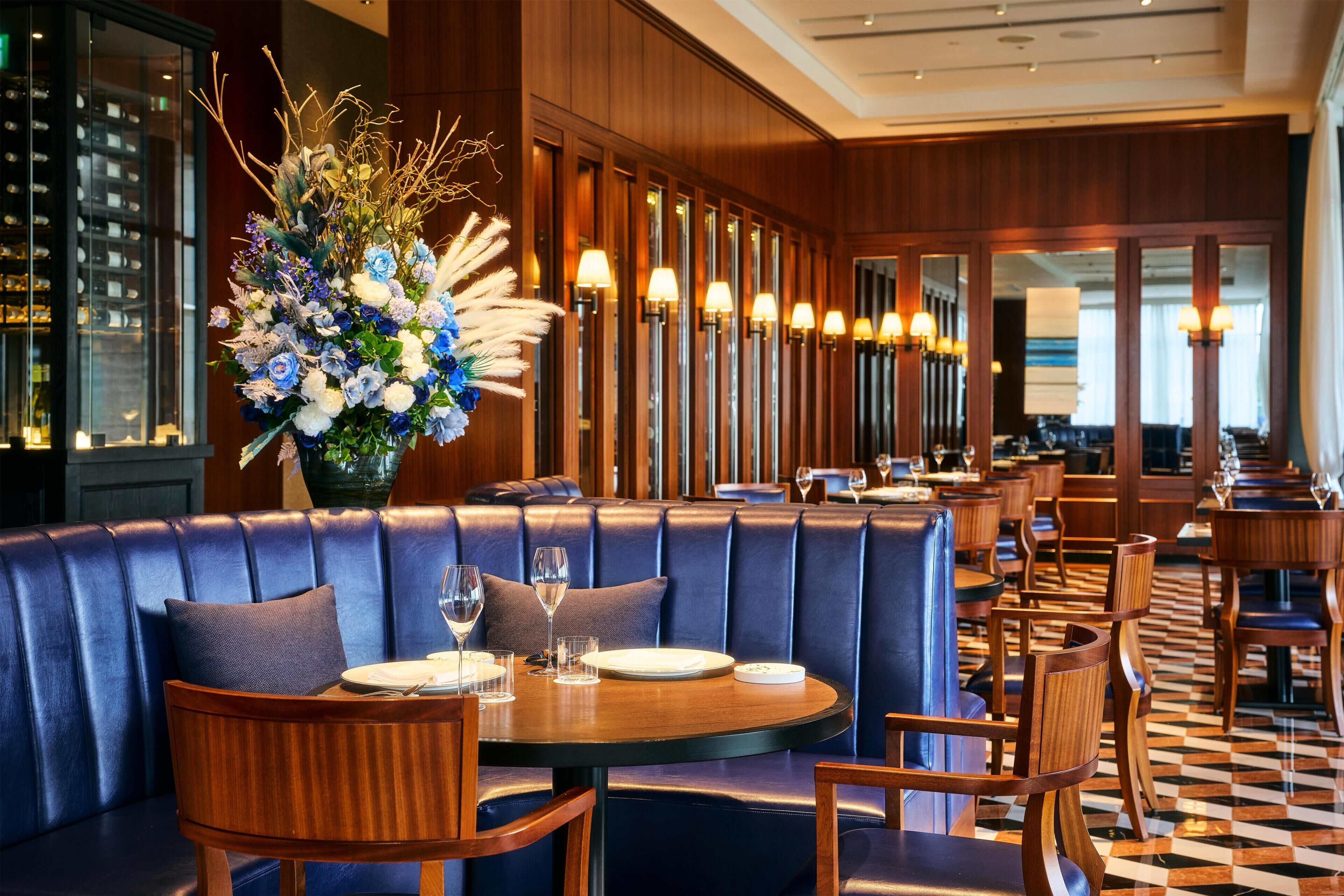 A restaurant with a blue leather booth, wooden tables, and chairs.