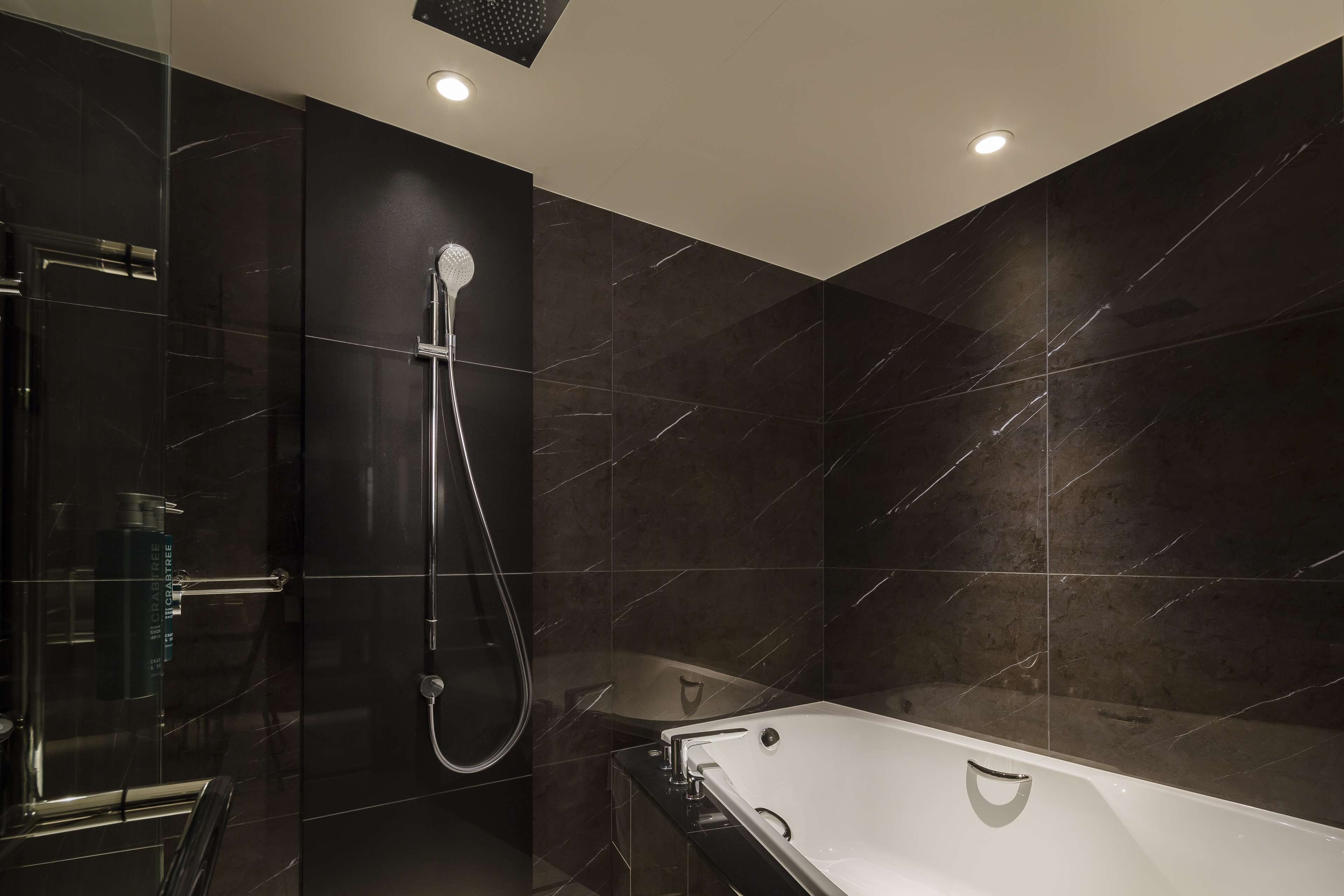 A modern bathroom with a glass-enclosed shower, a freestanding bathtub, and dark marble tiles.