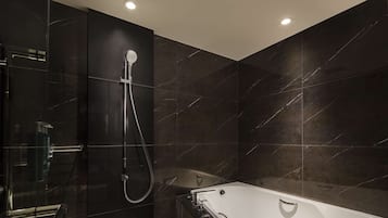 A modern bathroom with a glass-enclosed shower, a freestanding bathtub, and dark marble tiles.