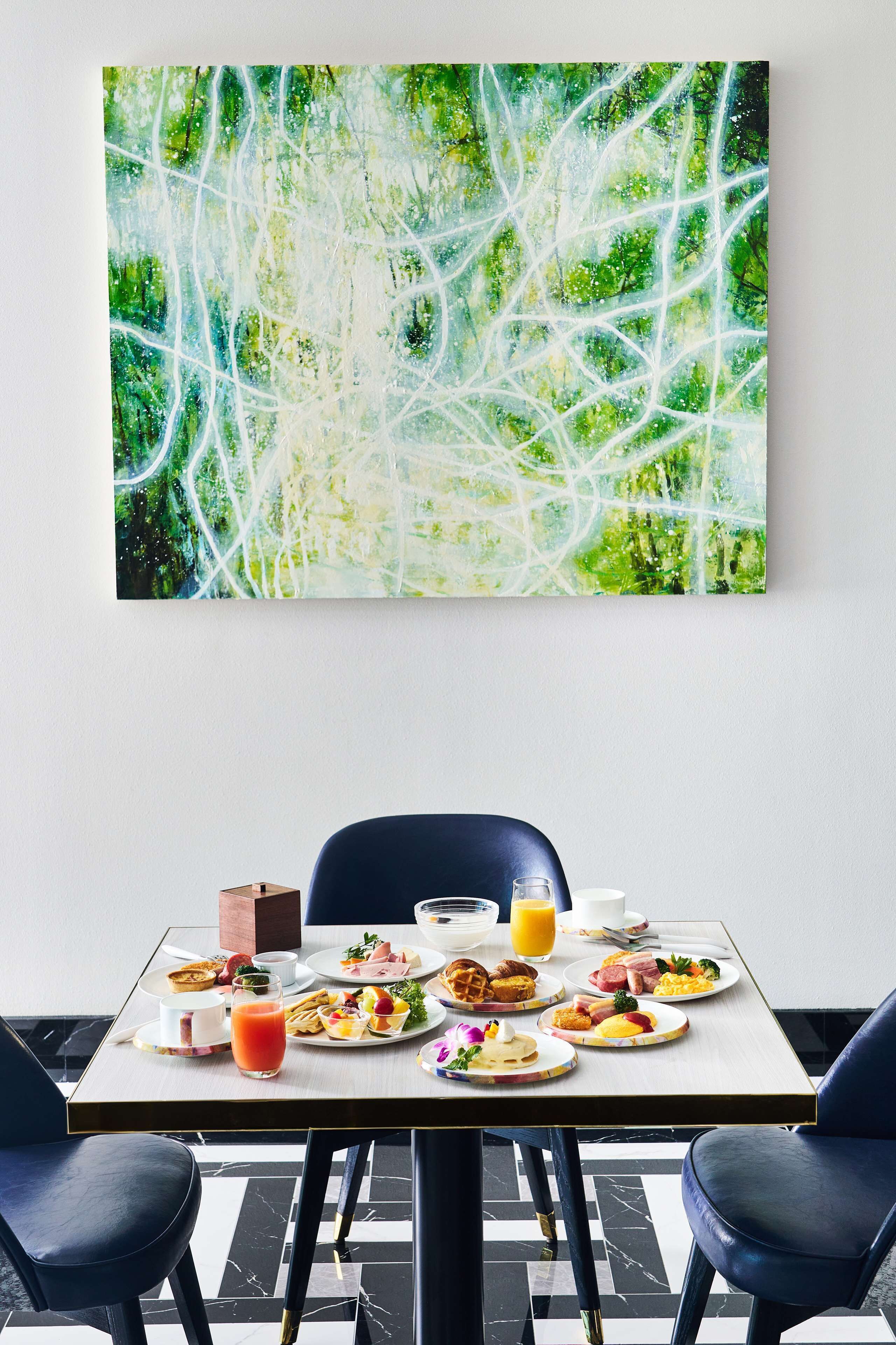 A dining table with breakfast items and a large abstract painting above it.
