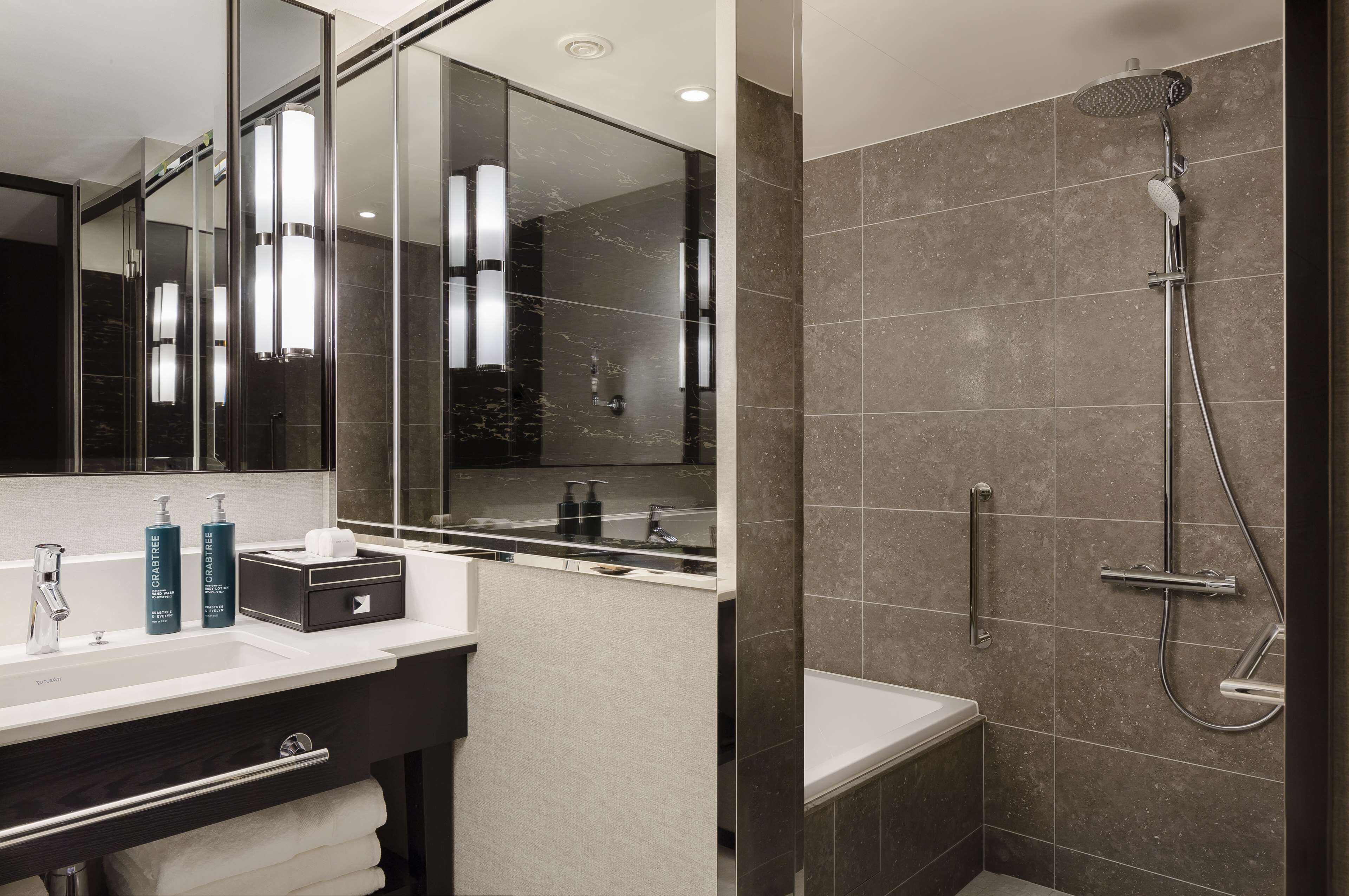 Une salle de bain moderne avec un grand miroir, un lavabo avec des articles de toilette et une douche équipée d’un pommeau de douche à main.