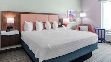 A hotel room with a large bed, a nightstand with a lamp, a chair, and a window with a view.