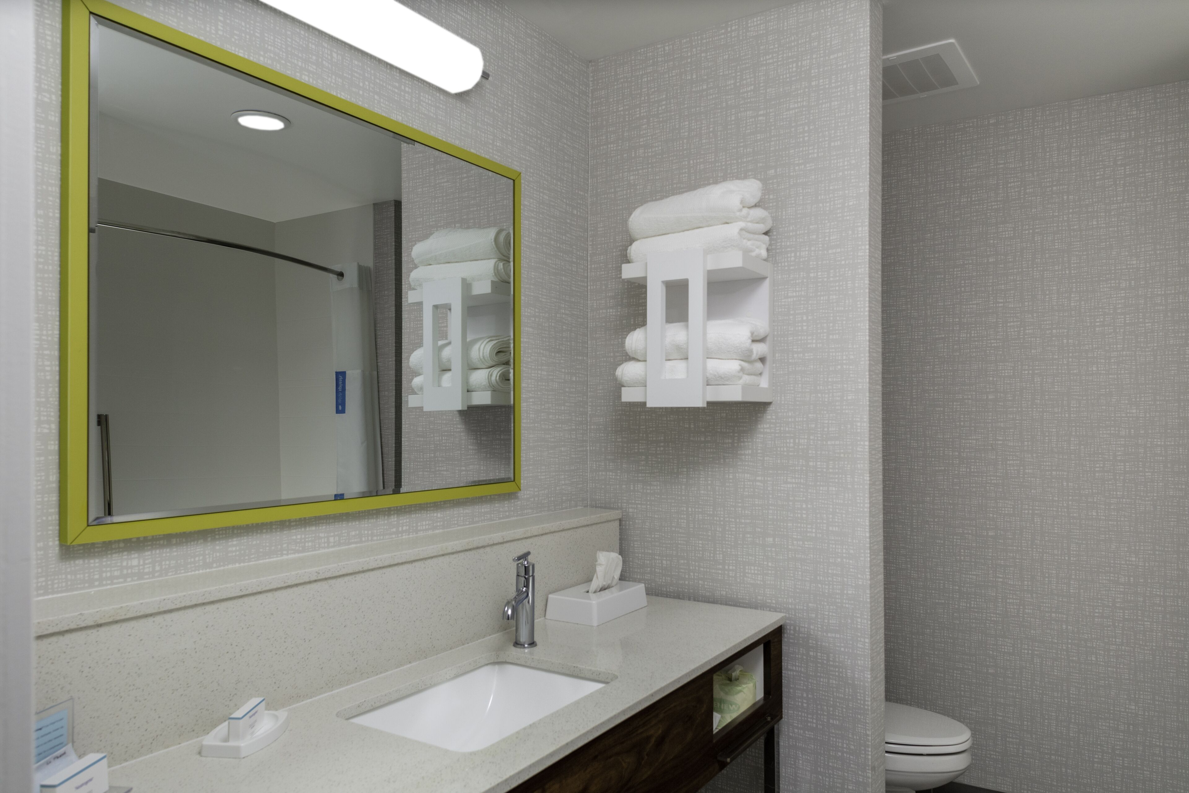 Une salle de bain avec un lavabo blanc, un miroir avec un cadre jaune et un porte-serviettes.