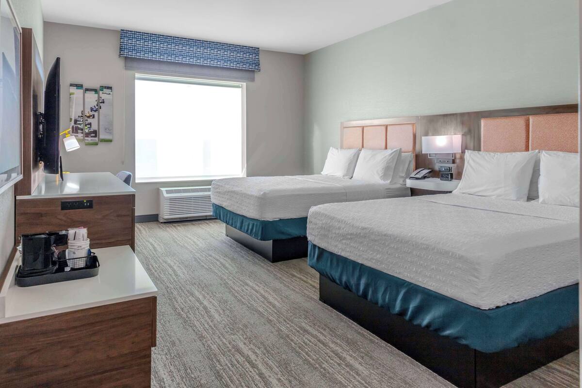 A hotel room with two beds, a desk with a computer and phone, a TV, and a window with blinds.