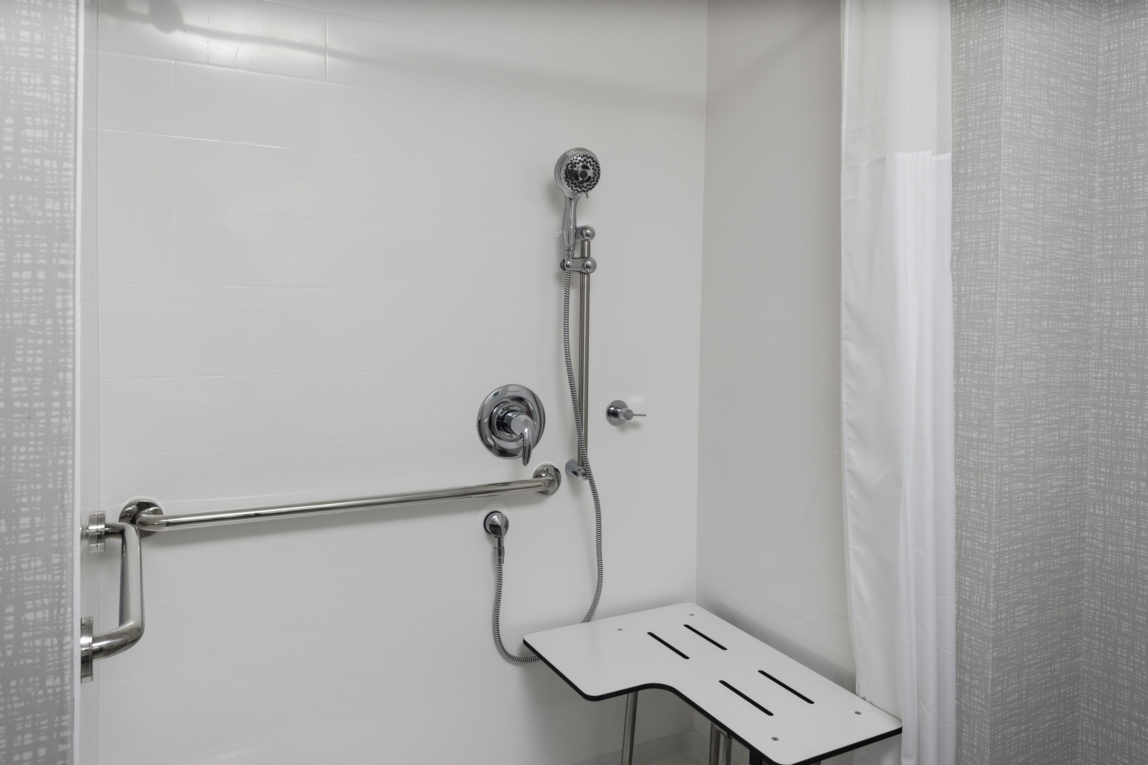 A shower area with a handheld showerhead, a handheld shower attachment, and a grab bar.