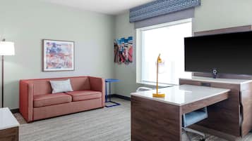 Une chambre d’hôtel moderne avec un canapé rouge, un bureau doté d’un téléviseur à écran plat et une grande fenêtre offrant une vue sur la ville.