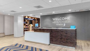 A hotel reception area with a modern design, including a reception desk, a wall-mounted sign, and a display of local attractions. - Hampton Inn & Suites Indianapolis West Speedway (Indianapolis)