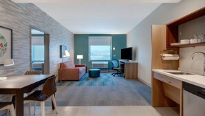 Ein modernes Hotelzimmer mit Essbereich, einer Couch, einem Fernseher und einer Küche inklusive Geschirrspüler.