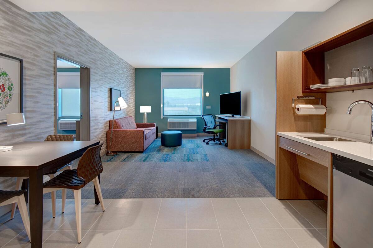 Una habitación de hotel moderna con comedor, sofá, televisor y cocina equipada con lavavajillas.