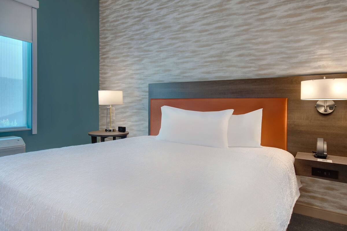 Una cama grande con cabecera de madera, dos mesitas de noche con lámparas y una pared con textura.