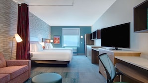 Ein Hotelzimmer mit Bett, Schreibtisch, Stuhl, Fernseher und einer Sitzecke.
