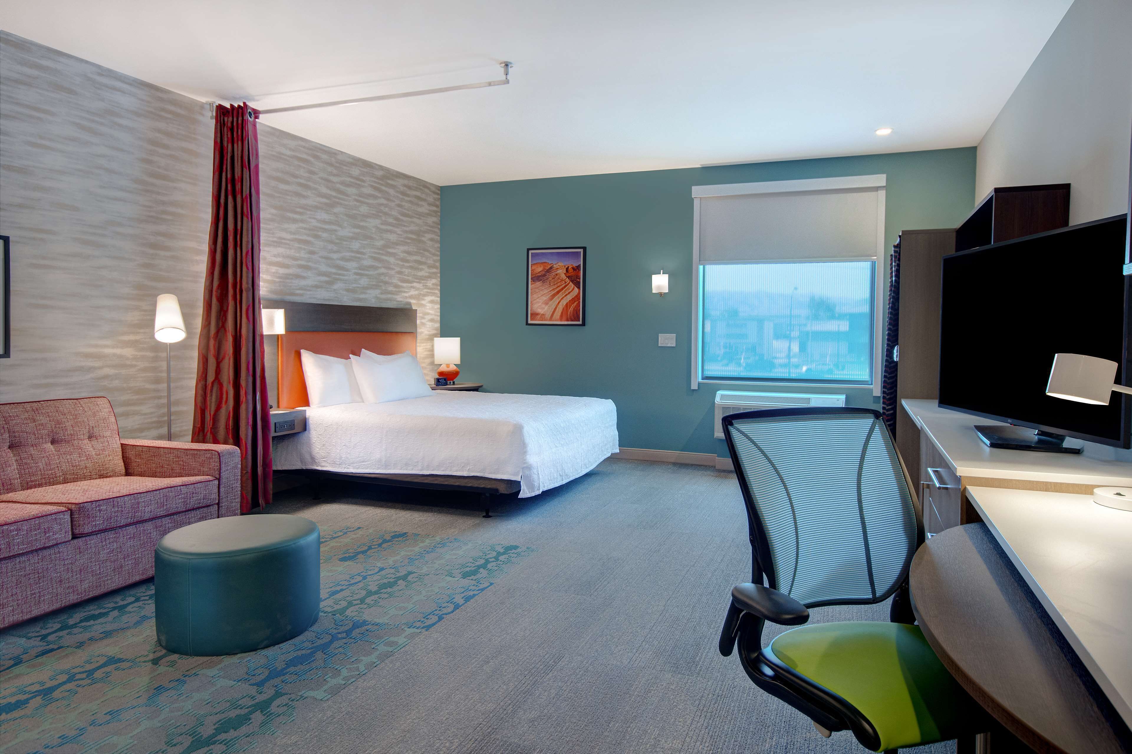 Una habitación de hotel con cama, escritorio, sillón, sofá y un amplio ventanal.