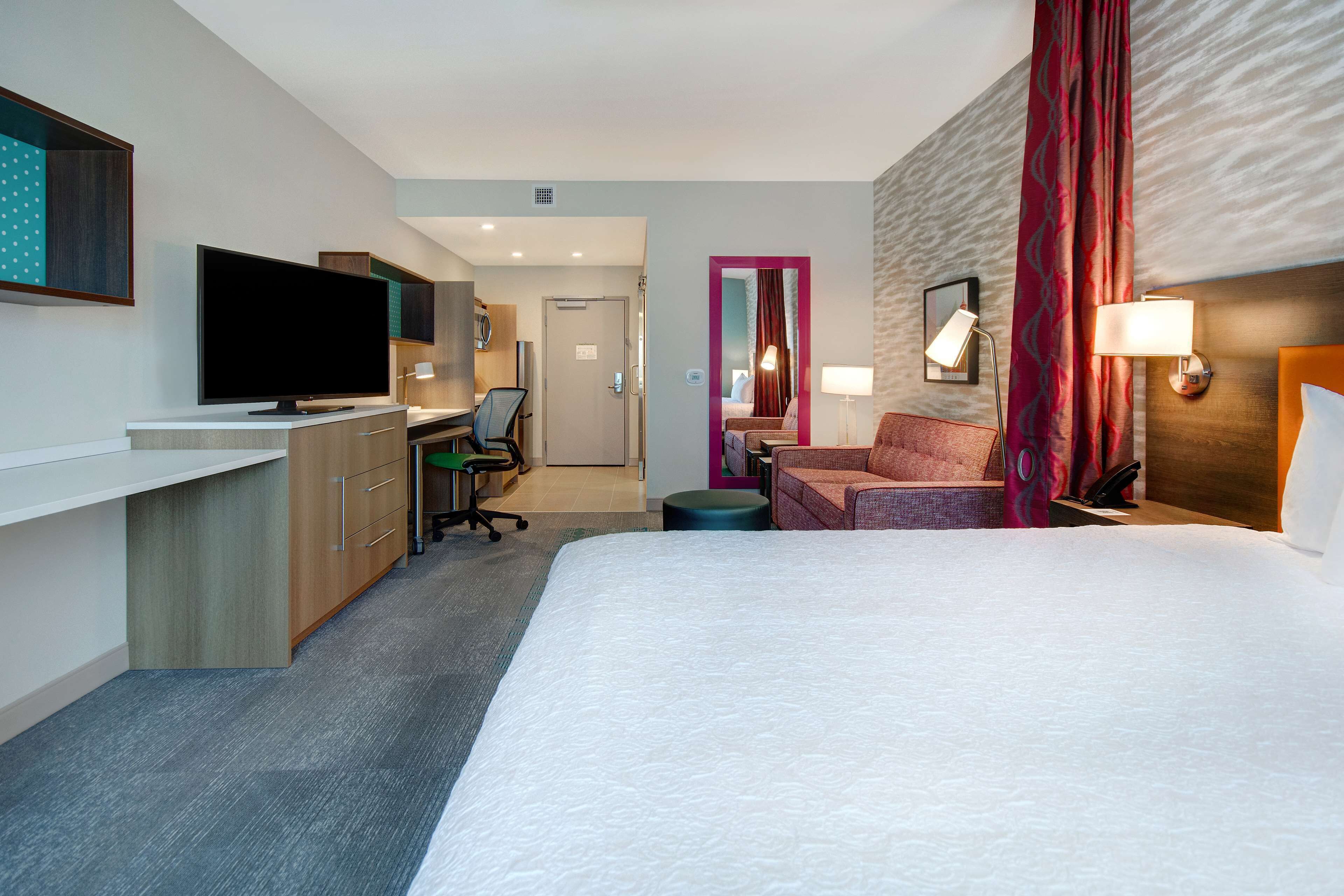 Ein Hotelzimmer mit einem großen Bett, einem Schreibtisch mit Flachbildfernseher, einer Couch und einer separaten Sitzecke mit Sessel und Tisch.