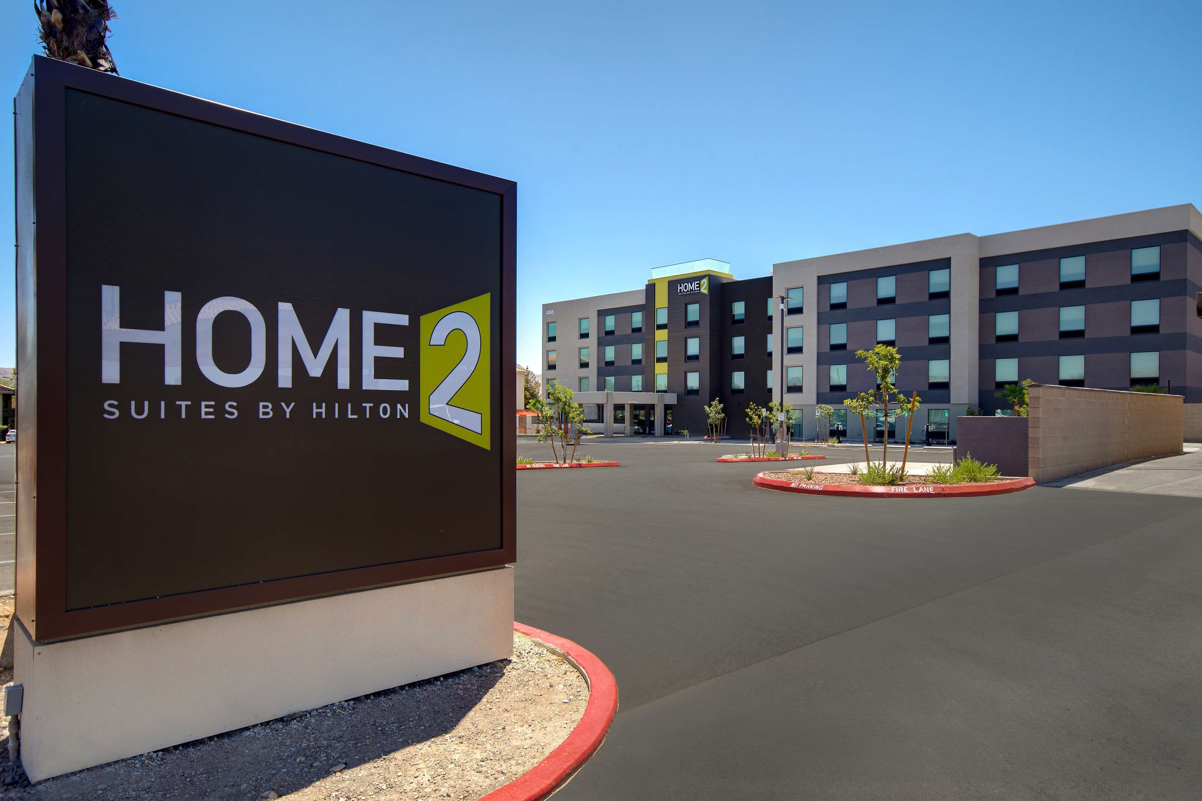 A sign for Home 2 Suites by Hilton, indicating a modern building with a parking lot and landscaping.