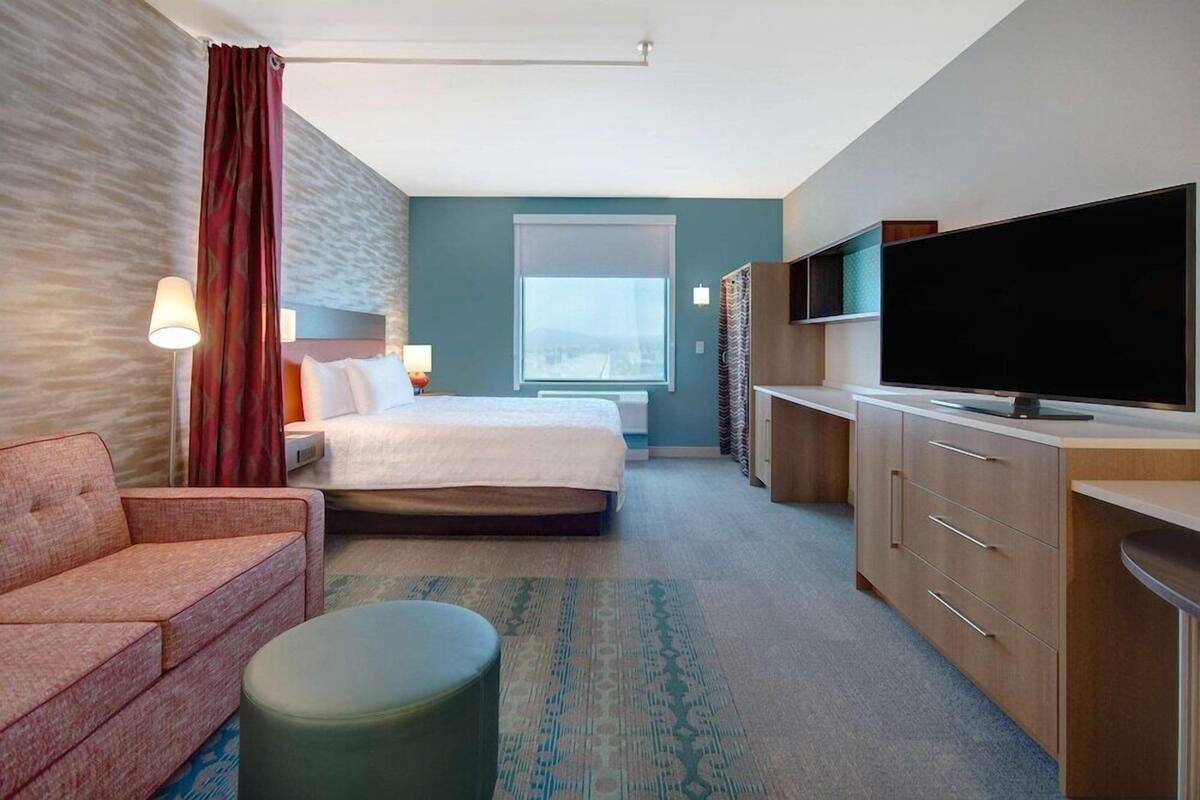 Una habitación de hotel con cama, sofá, televisión, escritorio y ventana.