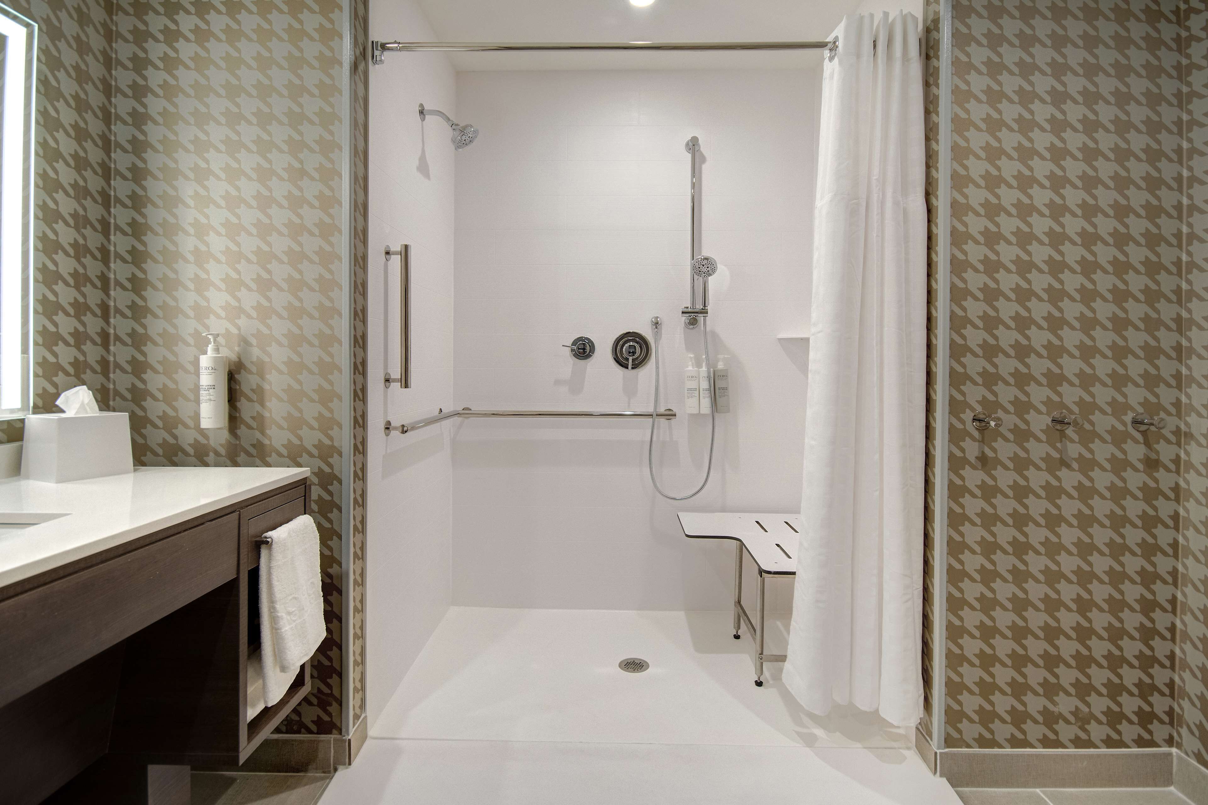 A modern bathroom with a shower, a vanity with a towel, and a patterned wall.