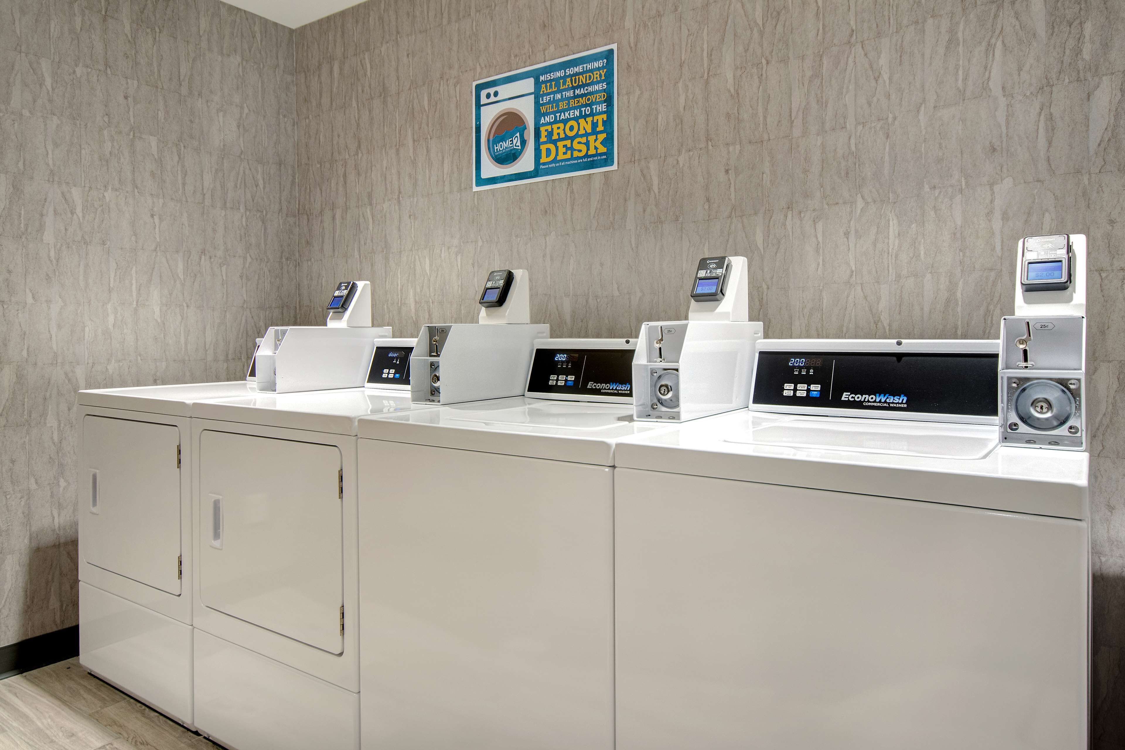 A laundry station with multiple washing machines and dryers, a sign above indicating missing items should be taken to the front desk, and a digital display on one machine.