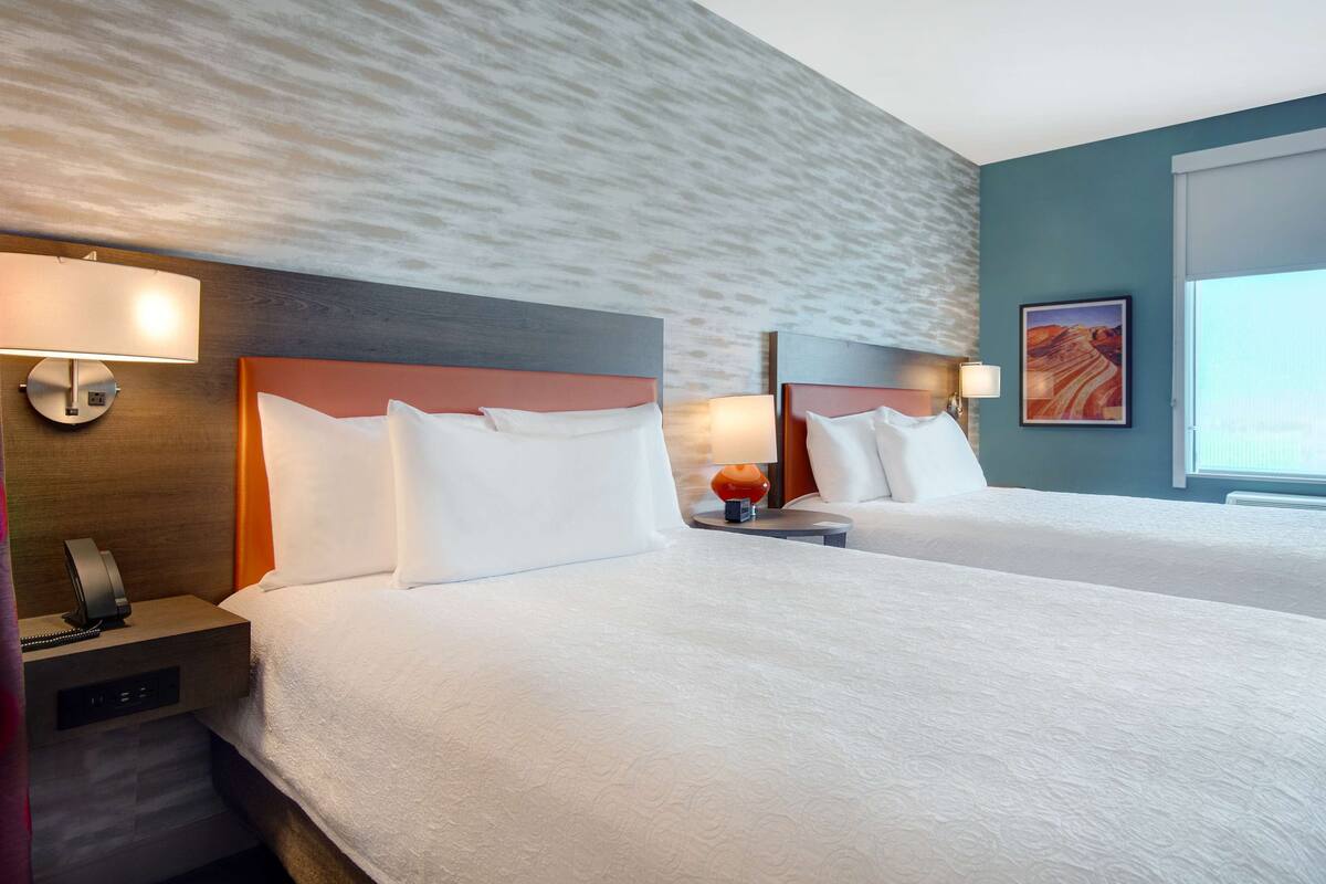 Habitación de hotel con dos camas, una mesita de noche con teléfono y una lámpara de pared.